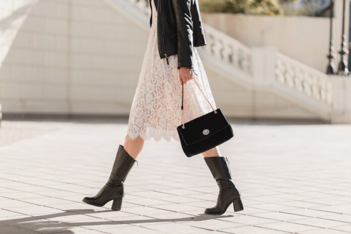 young pretty woman walking in street in fashionable outfit, holding purse, wearing black leather jacket and white lace dress, spring autumn style, warm sunny weather, romantic look