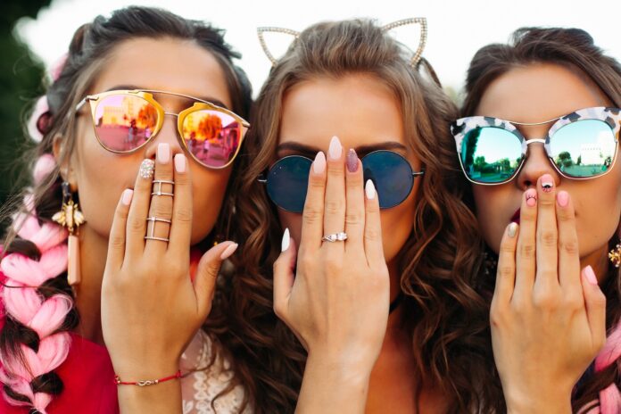 close-up-three-young-girls-wearing-creative-sunglasses-with-designed-manicure-two-lady-covers-mouth-one-hiding-face-by-hands-happy-friends-posing-having-fun-together